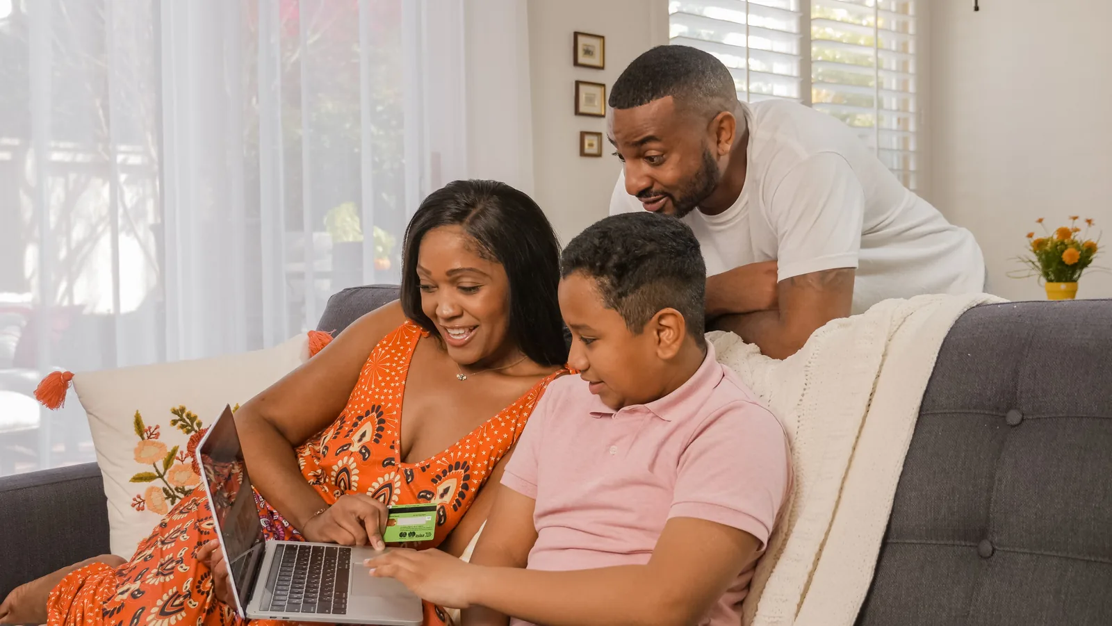 Família reunida no sofá vendo algo no notebook, com uma criança segurando o celular.