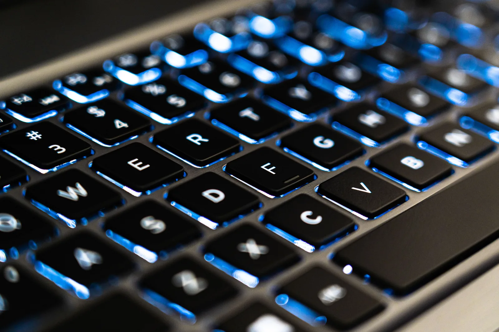 Teclado de notebook com iluminação azul em close, teclas em foco.